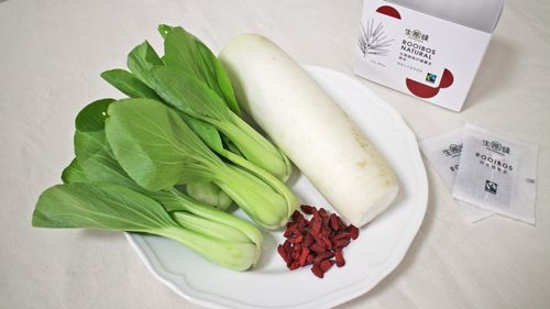 國寶茶原味一盒，旁邊擺兩個茶包，白色盤子上面擺著青江菜、白蘿蔔與枸杞